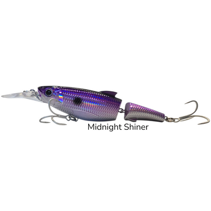 A hard bait fishing lure with a metallic purple and silver iridescent finish, featuring a diving lip, two treble hooks, and the text 'Midnight Shiner' printed below it on a plain white background. Purple Jerkbait Swimbait